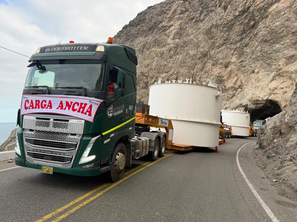 Tracto con letrero de carga ancha trasladando tanques junto a un túnel