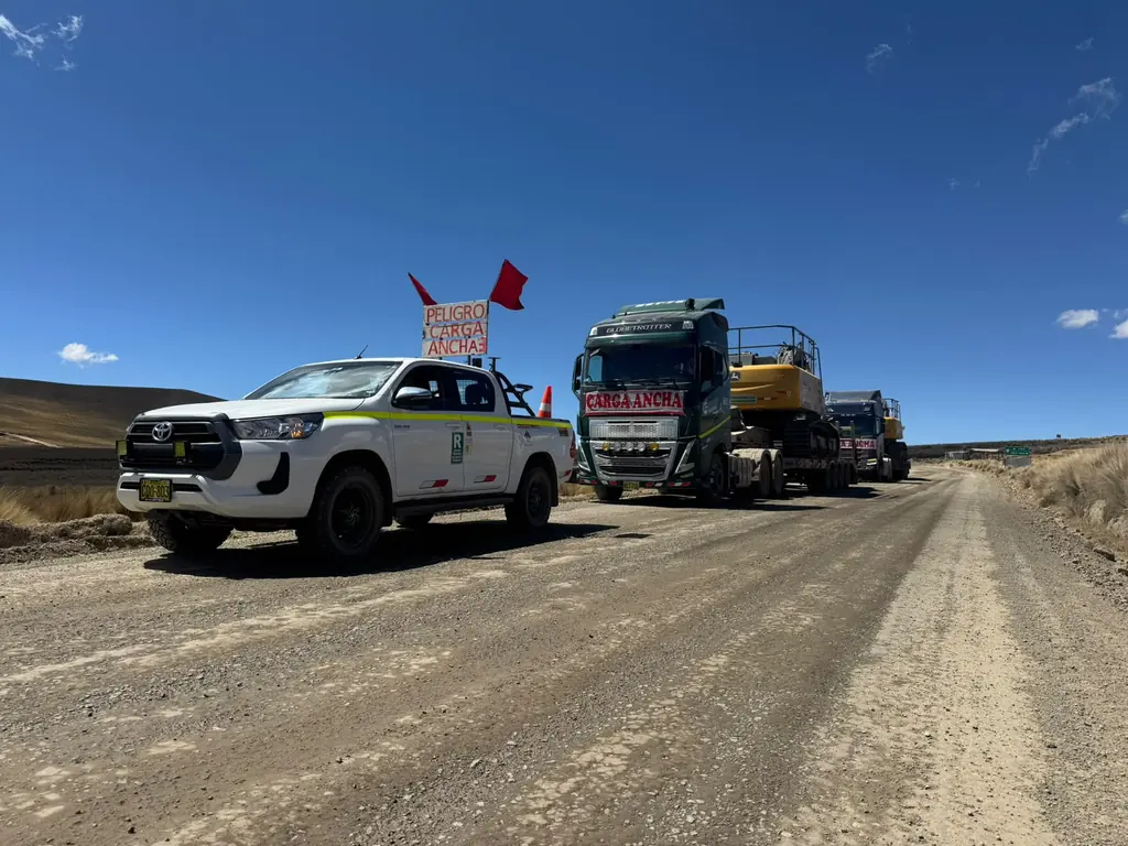 Camioneta de escolta delante de una cama baja con excavadora en vía afirmada