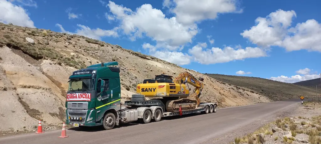 Convoy con excavadora sobre cama baja en carretera de altura